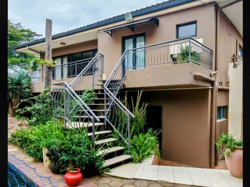 Rear exterior view featuring a swimming pool, paved patio area, and an elevated balcony accessible via an external metal staircase.