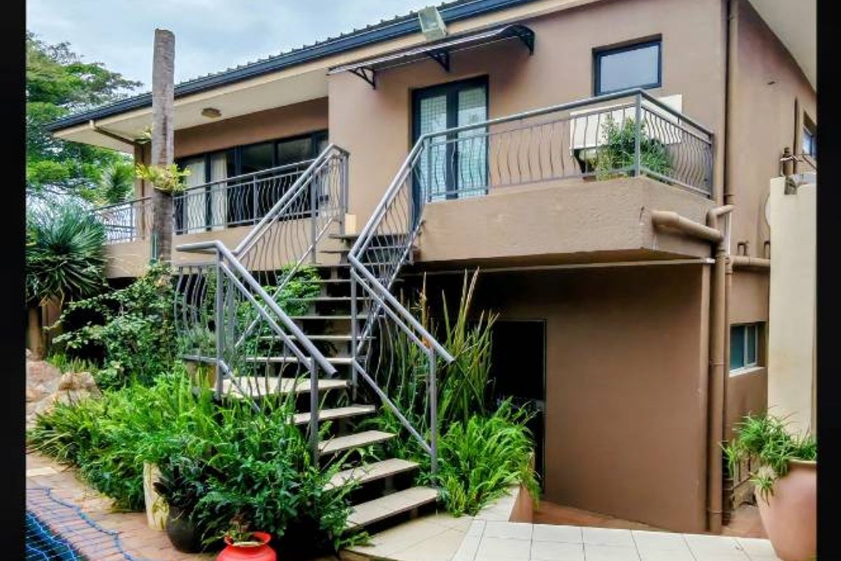 Rear exterior view featuring a swimming pool, paved patio area, and an elevated balcony accessible via an external metal staircase.