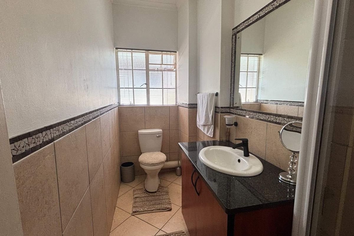 A functional bathroom featuring a granite-topped vanity, drop-in basin, toilet, and tiled walls with a decorative mosaic border.