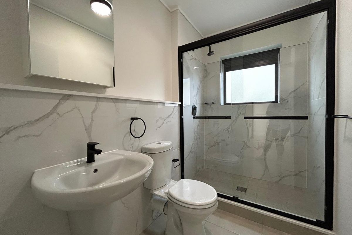 Modern bathroom featuring marble-look wall tiles, a glass-enclosed shower with black frame, pedestal basin, and contemporary black fixtures.
