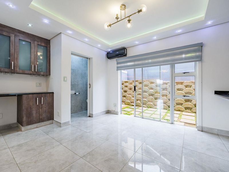 A bright, open-plan living area featuring modern tiled floors, recessed lighting, built-in cabinetry, and sliding glass doors leading to an outdoor space.