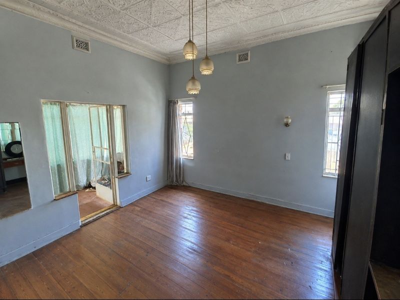 Spacious living area featuring original pressed metal ceilings, hardwood timber flooring, and large windows providing natural light, ready for renovation or modern styling.