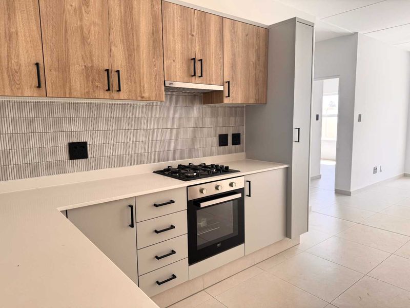 Modern kitchen featuring light wood-grain upper cabinets, grey lower cabinetry, stone countertops, gas hob, built-in oven, and a stylish vertical tile backsplash.