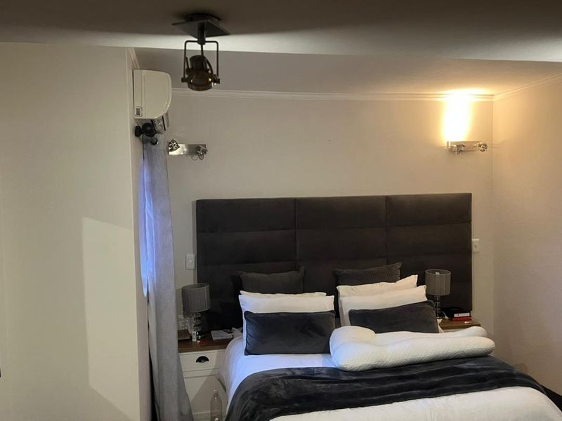 A well-maintained bedroom featuring a large upholstered headboard, wall-mounted air conditioning unit, and modern wall sconce lighting.