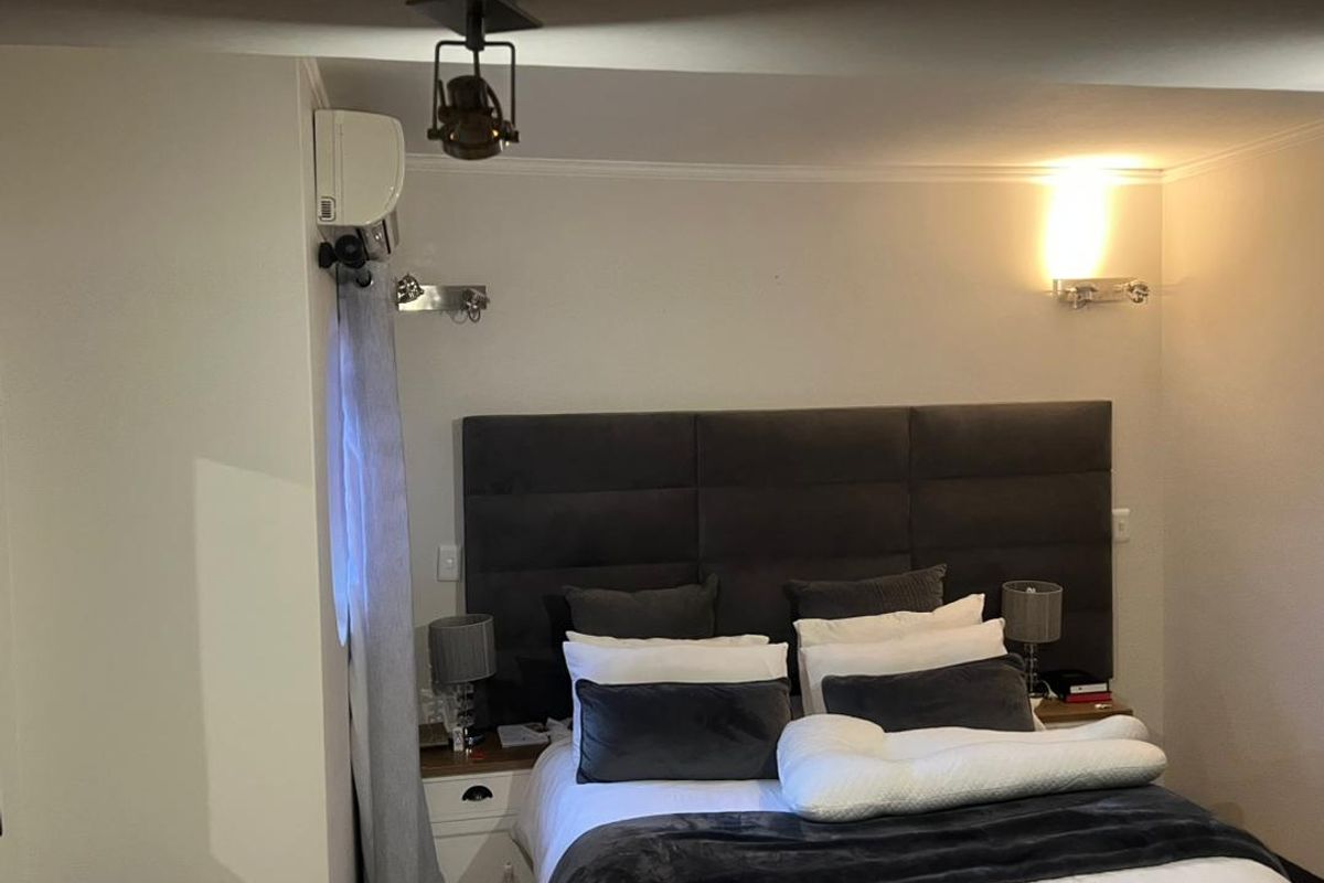 A well-maintained bedroom featuring a large upholstered headboard, wall-mounted air conditioning unit, and modern wall sconce lighting.