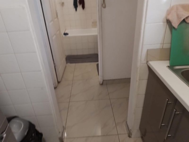 A view from a kitchen area looking into a small bathroom featuring tiled finishes and a standard bathtub.