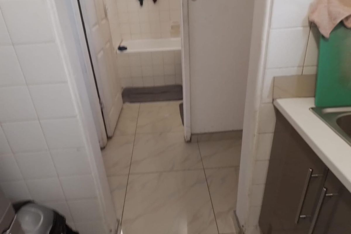 A view from a kitchen area looking into a small bathroom featuring tiled finishes and a standard bathtub.