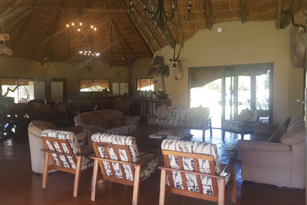 Spacious living area featuring a traditional thatched roof with exposed timber rafters, tiled flooring, and a built-in bar, opening to outdoor spaces.