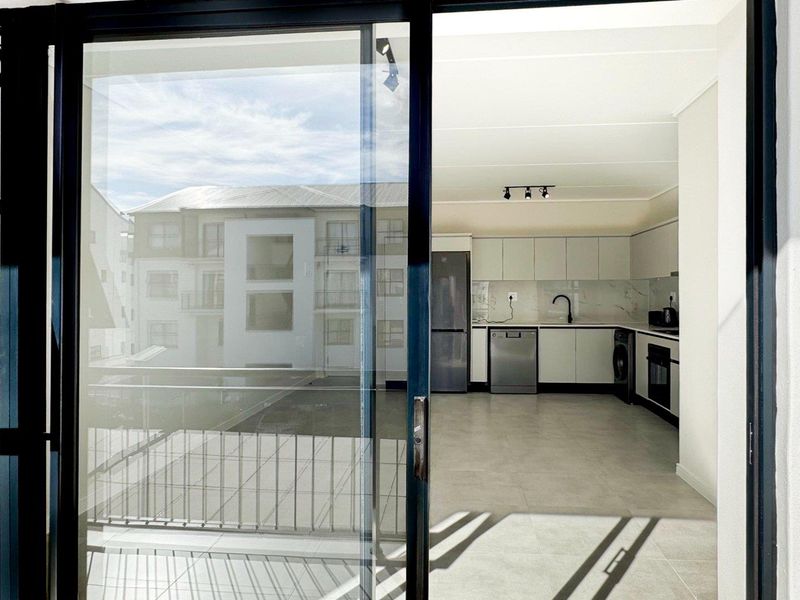 Modern open-plan kitchen and living area featuring sleek cabinetry, integrated appliances, and large sliding doors leading to a balcony.