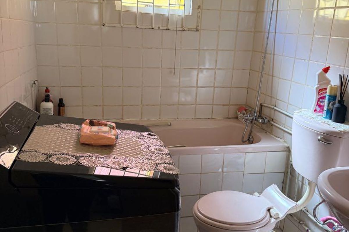 A compact bathroom featuring a vintage pink bathtub and toilet suite, tiled walls, and a window with security bars.