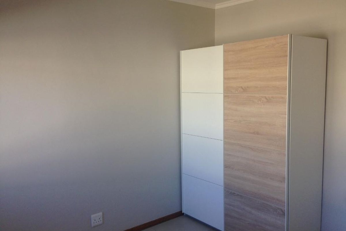 A bedroom featuring neutral wall tones, tiled flooring, and a modern built-in wardrobe with a two-tone wood and white finish.