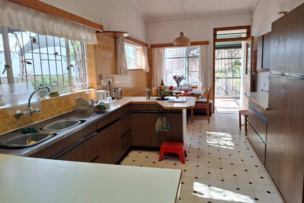 A dated kitchen featuring original laminate cabinetry, tiled backsplash, and vinyl flooring, offering significant potential for a modern renovation.