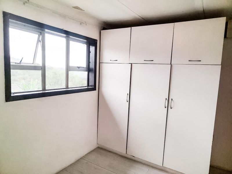A bedroom featuring a built-in wardrobe and an aluminium-framed window, showing signs of wear on the ceiling.
