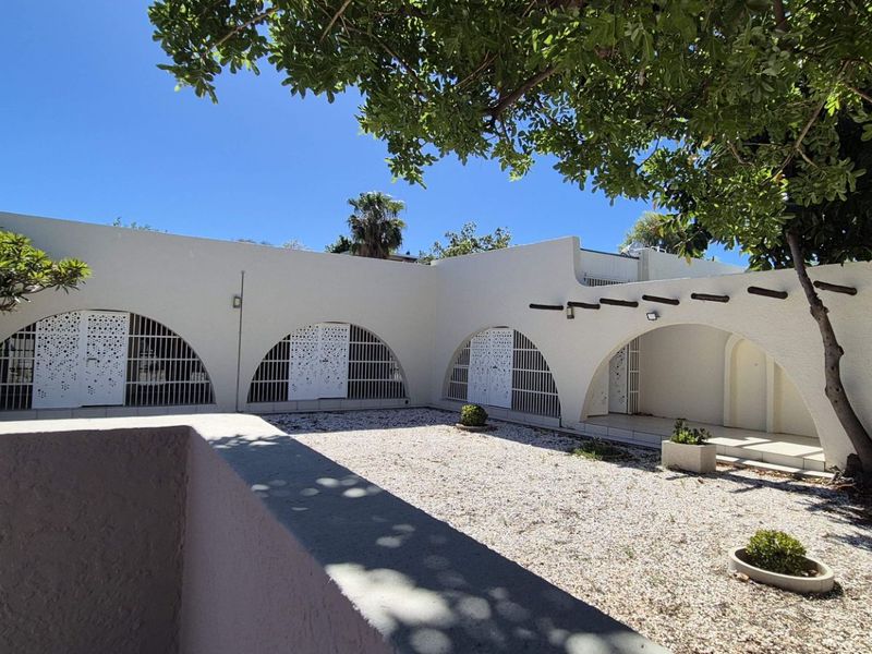A private rear courtyard featuring distinctive arched architectural elements, security gates, and a low-maintenance gravel surface with established trees.