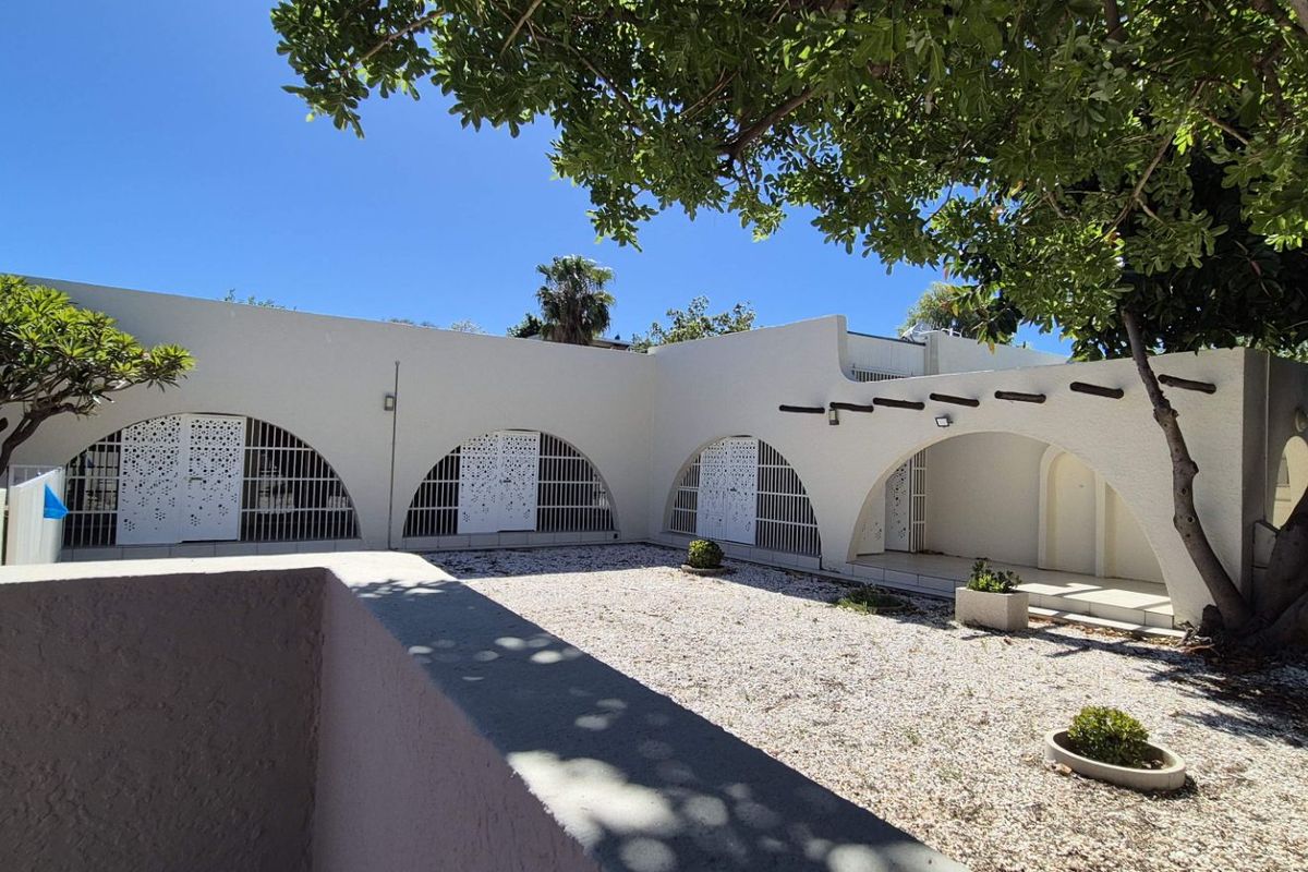 A private rear courtyard featuring distinctive arched architectural elements, security gates, and a low-maintenance gravel surface with established trees.