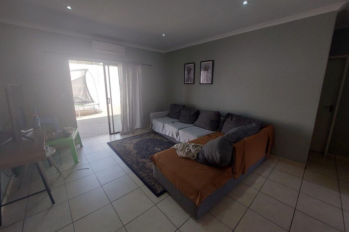 A living room featuring tiled flooring, recessed ceiling lighting, and a wall-mounted air conditioning unit, with sliding glass doors leading to an outdoor area.