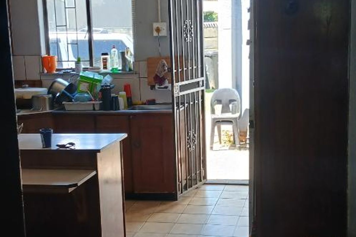 A functional kitchen area featuring tiled flooring, built-in cabinetry, and direct access to the exterior through a security gate.