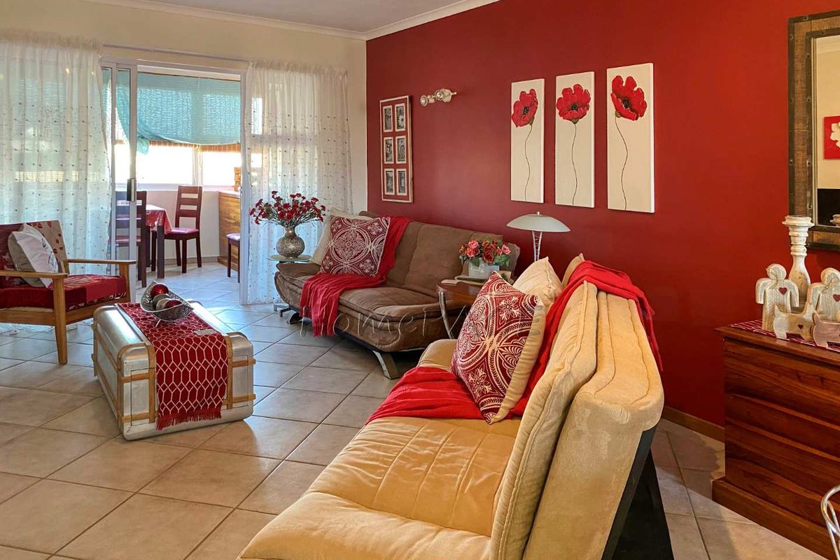 A bright living room featuring tiled flooring and a sliding glass door leading to an enclosed balcony area.