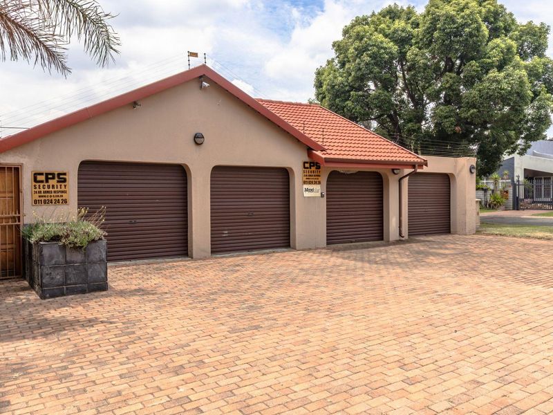 A triple garage with roll-up doors and a paved driveway, featuring perimeter security fencing and a secure pedestrian gate.