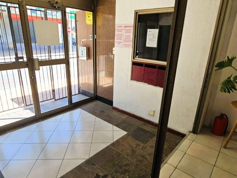 Apartment building entrance lobby featuring a secure metal gate, glass door, and built-in mailboxes with tiled flooring.