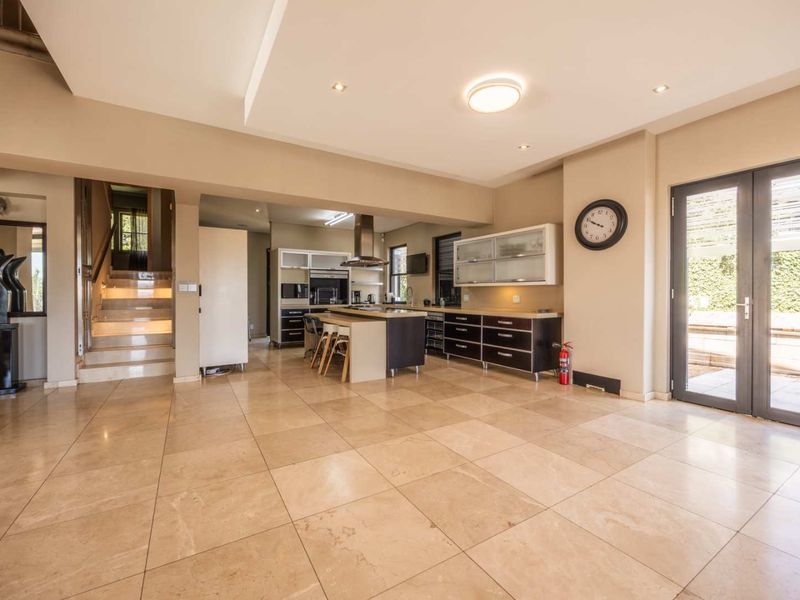 Spacious open-plan living area featuring stone flooring, a modern kitchen with island, and a staircase with integrated lighting leading to the upper level.
