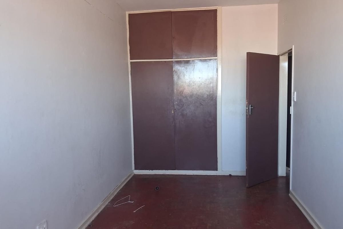 An empty bedroom featuring built-in cupboards and original wooden flooring, offering a blank canvas for renovation or interior design updates.