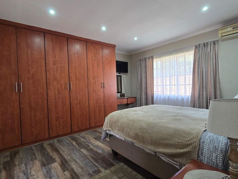 A well-maintained bedroom featuring extensive built-in wooden cupboards, recessed ceiling lighting, an air conditioning unit, and durable laminate flooring.