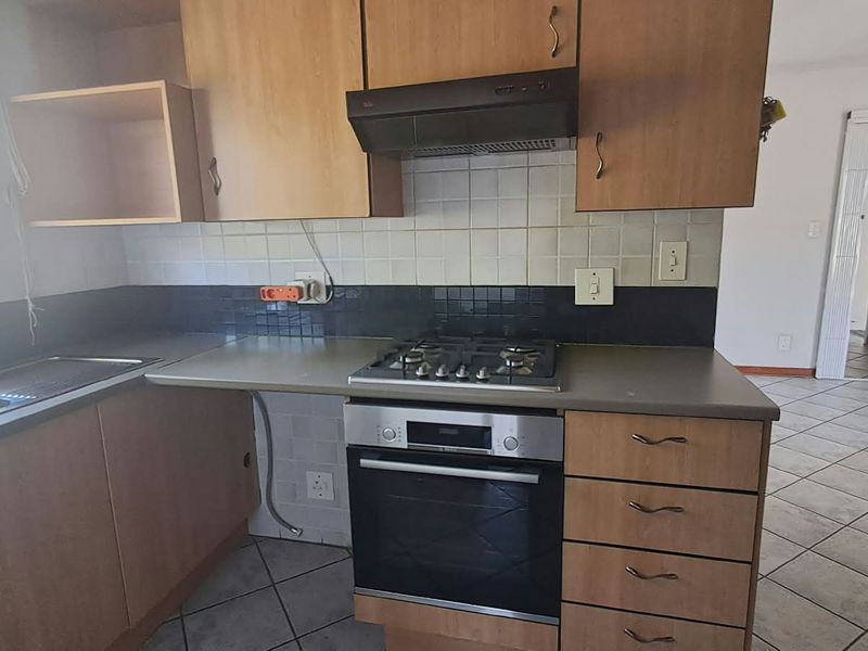 Functional kitchen featuring built-in cabinetry, gas hob, oven, extractor fan, and double sink with tiled backsplash and flooring.