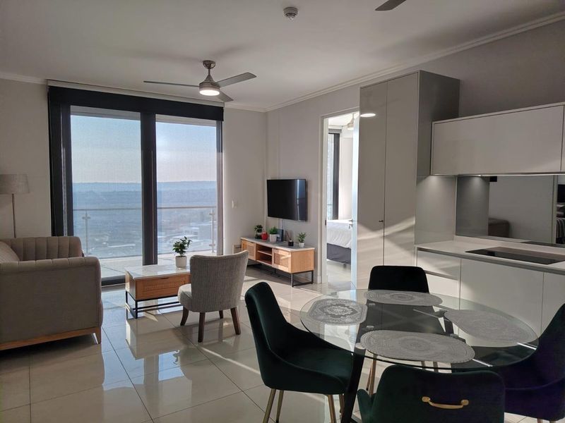 Modern open-plan living area featuring sleek kitchen cabinetry, tiled floors, ceiling fans, and large sliding doors leading to a balcony with expansive views.