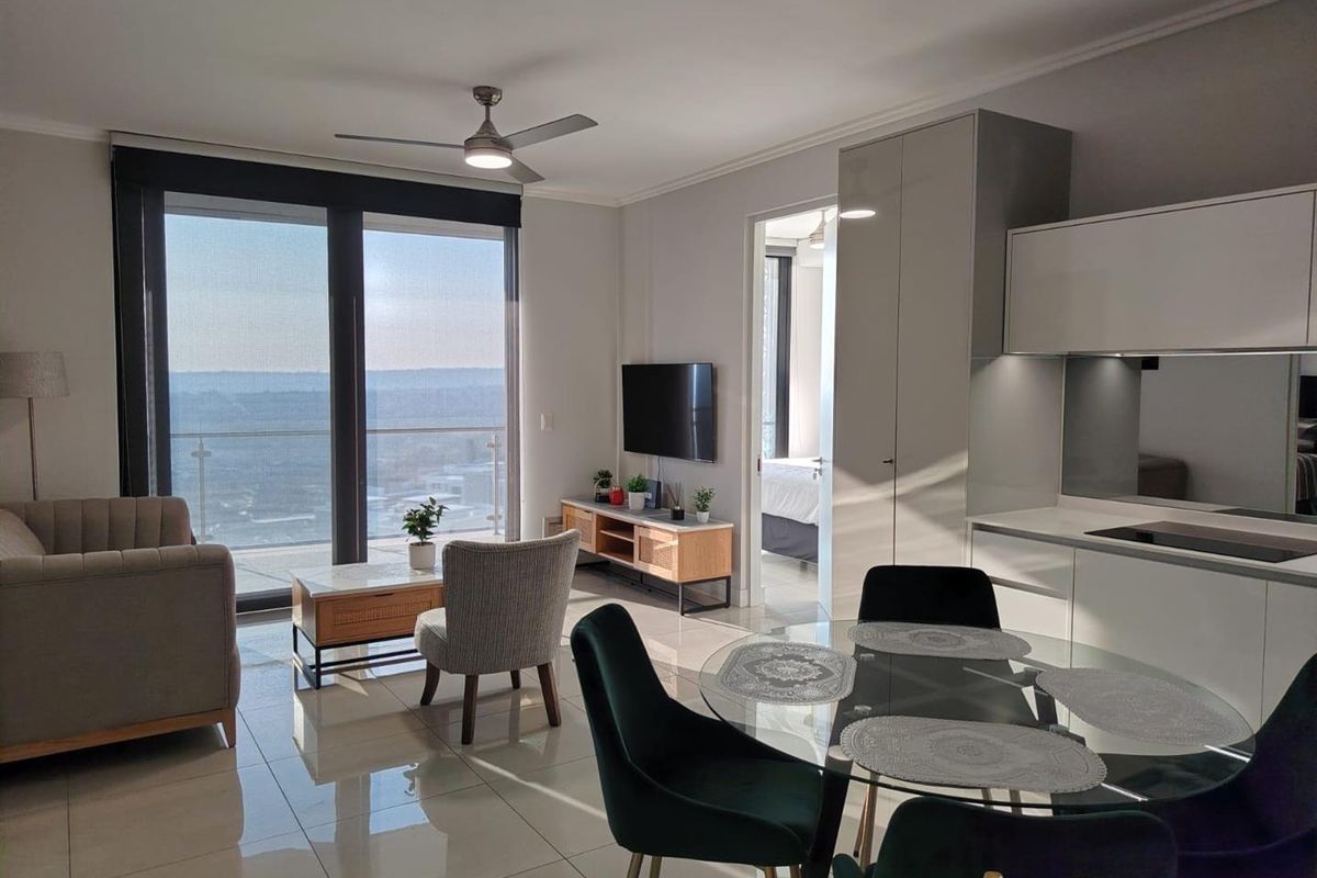 Modern open-plan living area featuring sleek kitchen cabinetry, tiled floors, ceiling fans, and large sliding doors leading to a balcony with expansive views.