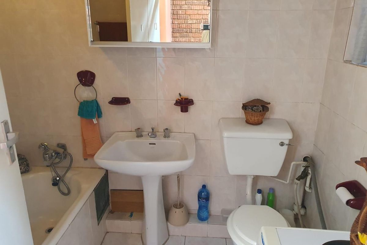 A functional bathroom featuring a pedestal basin, standard toilet, and a bathtub with a shower mixer, finished with neutral wall and floor tiling.