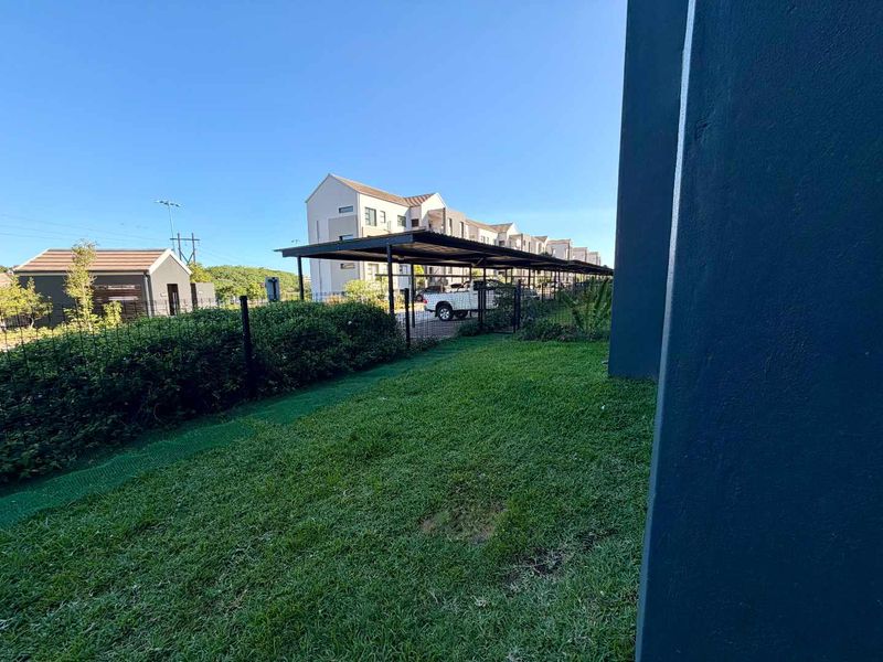 A view of the rear garden area featuring a well-maintained lawn, perimeter wire fencing, and a covered carport structure.