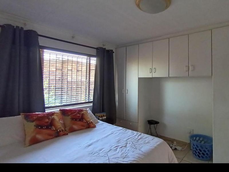 A bedroom featuring built-in cupboards, tiled flooring, and a window with blinds, offering a functional and well-lit living space.
