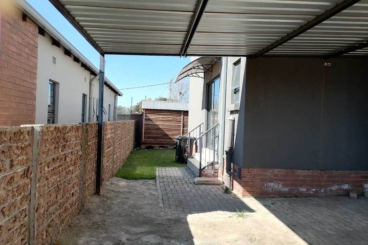 A rear exterior view of the townhouse featuring a covered patio area, paved walkway, and a small garden space enclosed by a brick boundary wall.