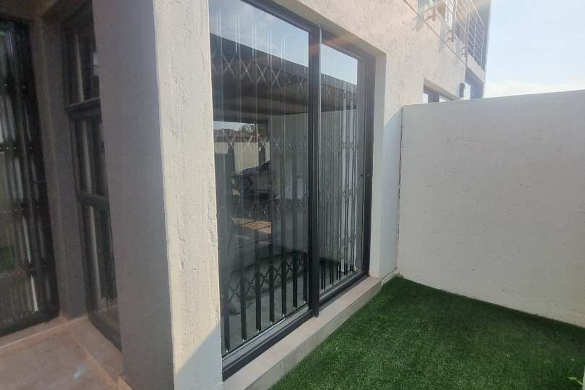 Rear exterior view of the apartment featuring a small artificial turf garden, sliding glass doors with security gates, and modern external wall lighting.