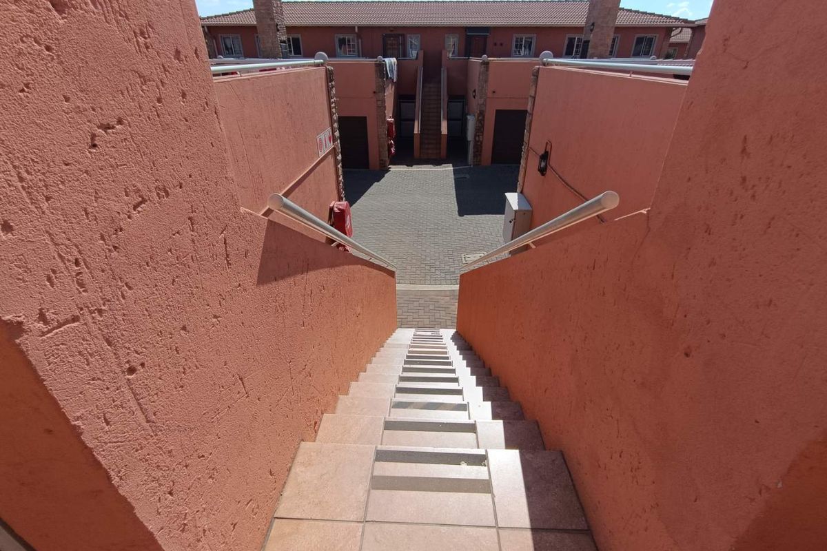 An exterior view looking down a tiled staircase towards a paved courtyard area within a townhouse complex.