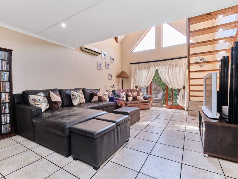 Spacious living room featuring high vaulted ceilings, tiled flooring, a timber staircase, and large windows providing ample natural light and access to the outdoors.