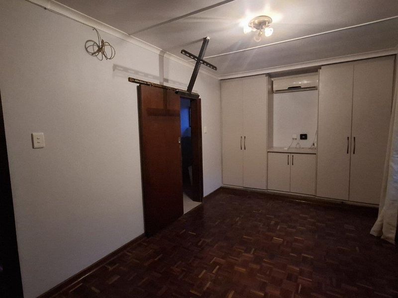 A bedroom featuring parquet flooring, built-in cupboards, and an integrated air conditioning unit, presenting a functional space ready for personalization.