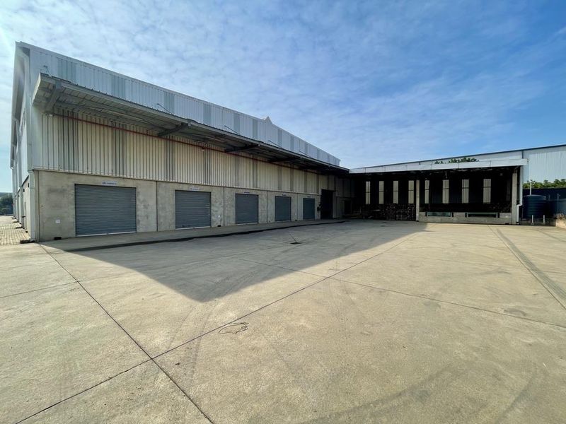 Industrial warehouse exterior featuring a large concrete yard, multiple roller shutter doors, and a covered loading bay area.