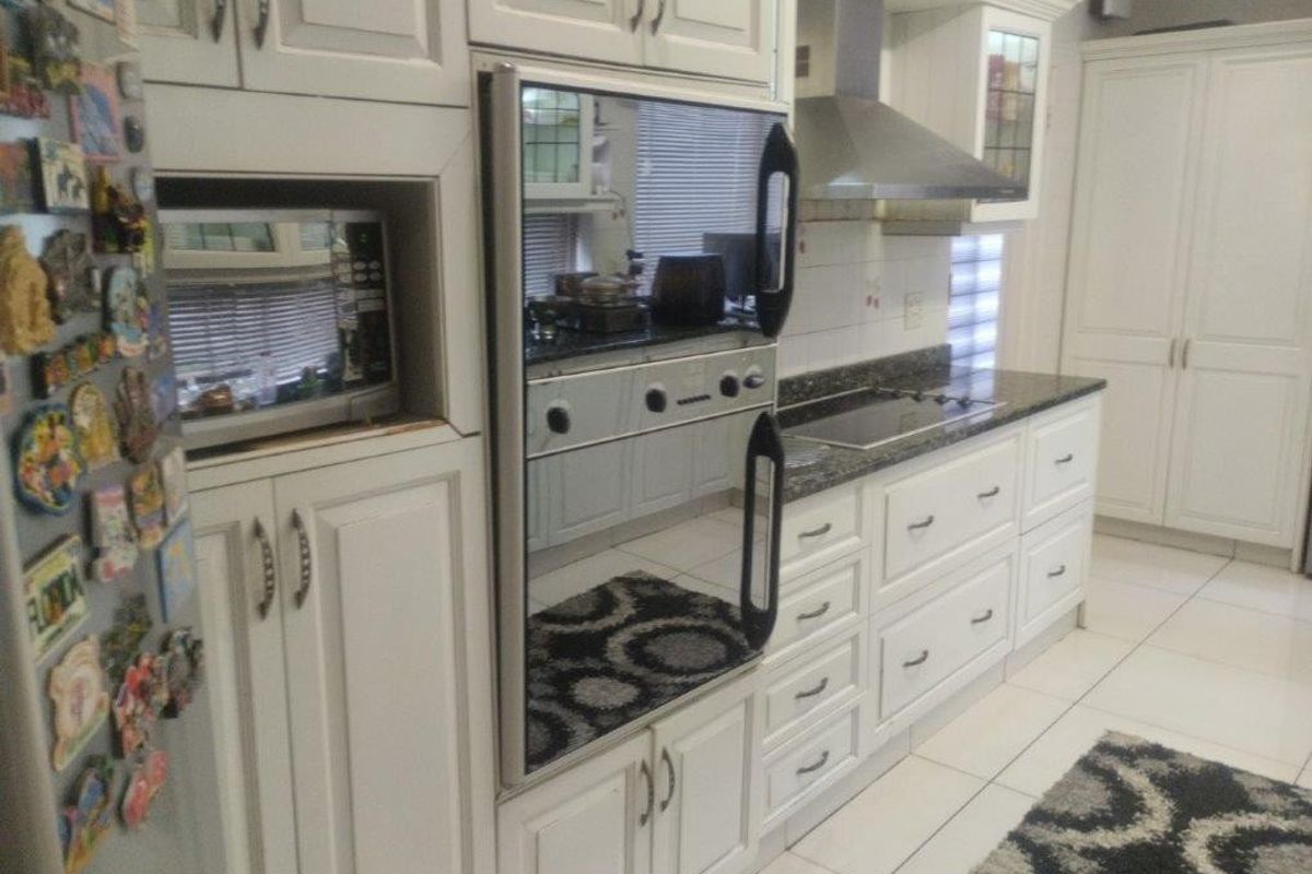 A functional kitchen featuring white cabinetry, granite countertops, integrated appliances including an oven and hob, and tiled flooring.