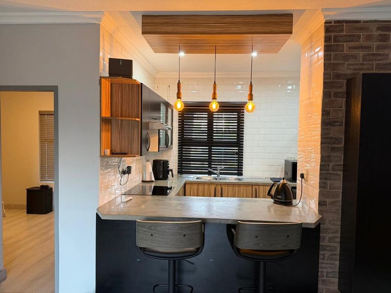 Modern kitchen featuring a concrete breakfast bar, subway tile backsplash, exposed brick accents, and custom timber ceiling detailing with pendant lighting.