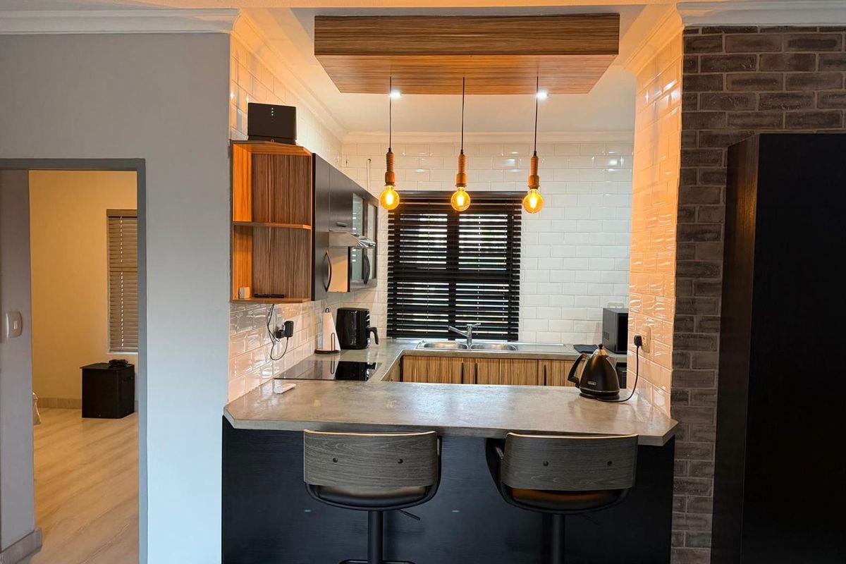 Modern kitchen featuring a concrete breakfast bar, subway tile backsplash, exposed brick accents, and custom timber ceiling detailing with pendant lighting.