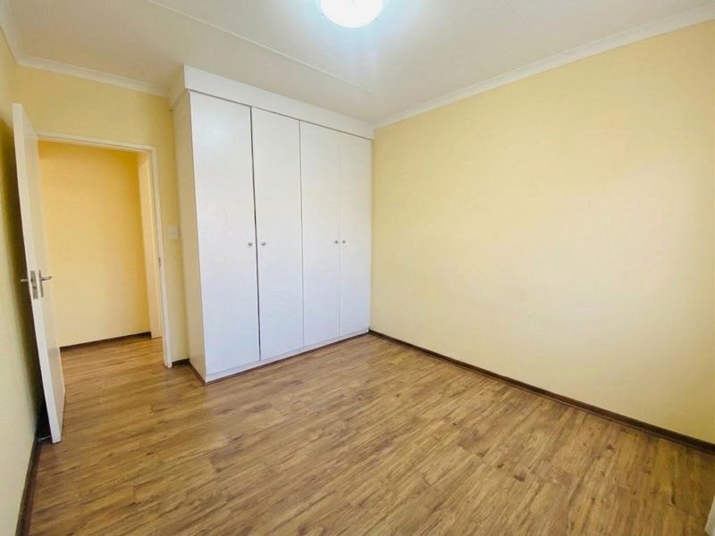 A clean, empty bedroom featuring laminate flooring, neutral walls, and a built-in wardrobe, offering a blank canvas for personalization.