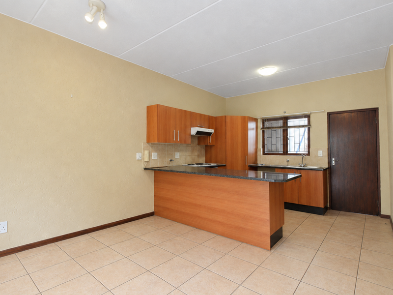 An open-plan kitchen featuring wooden cabinetry, granite countertops, a breakfast bar, and tiled flooring, presented in a clean, vacant condition.