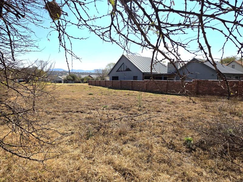 A view of a vacant residential plot featuring a brick boundary wall and surrounding neighborhood context.