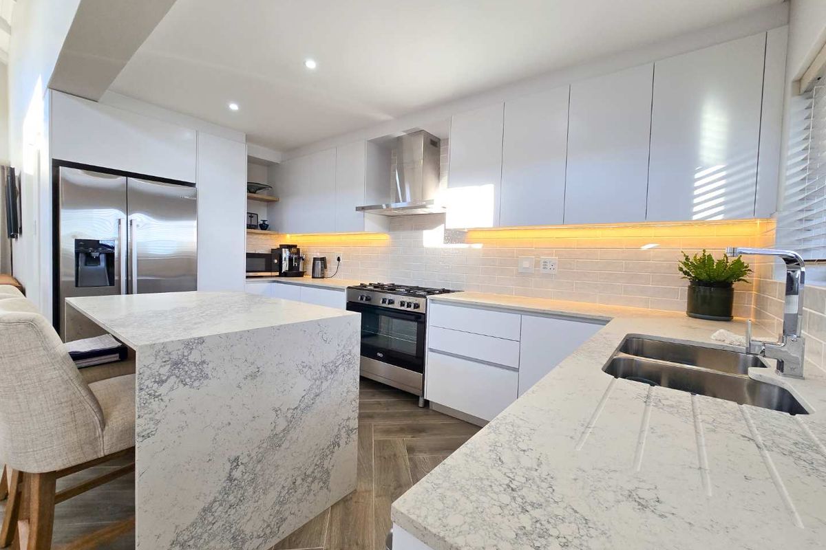 Modern kitchen featuring sleek white cabinetry, stone countertops, a central island, stainless steel gas stove, and integrated lighting.