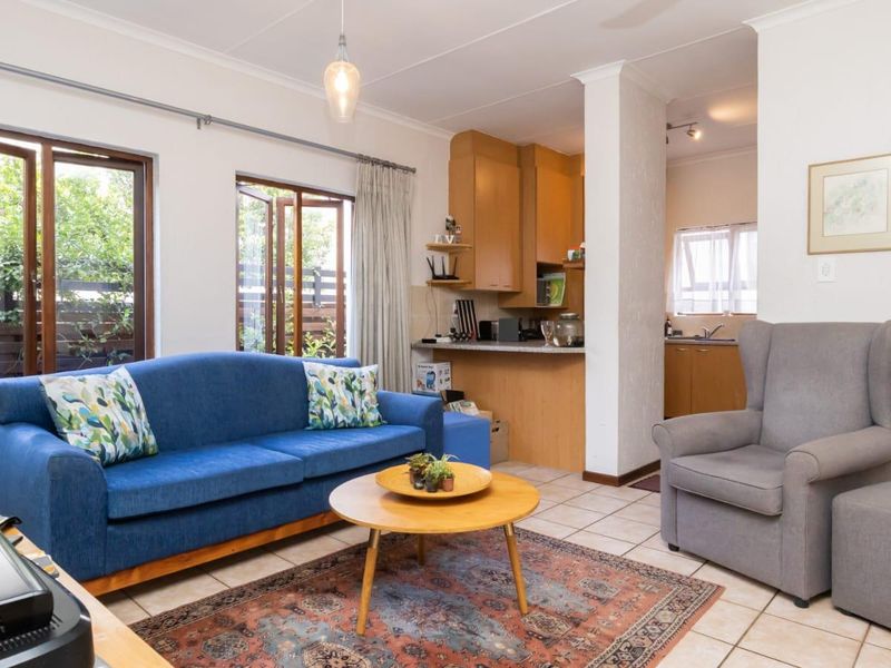 Open-plan living area featuring tiled floors, wooden window frames, and an adjoining kitchen with built-in cabinetry, creating a functional and connected living space.