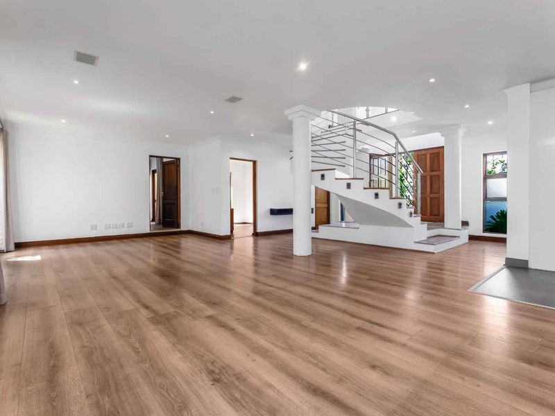 Spacious open-plan living area featuring modern laminate flooring, recessed lighting, and a prominent central staircase with a stainless steel balustrade.