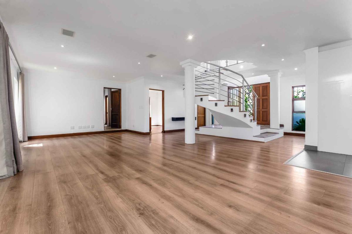 Spacious open-plan living area featuring modern laminate flooring, recessed lighting, and a prominent central staircase with a stainless steel balustrade.