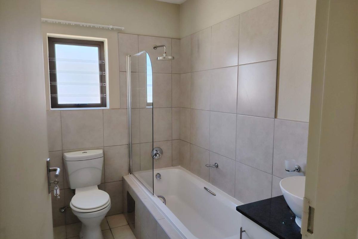 A clean, functional bathroom featuring a bathtub with a glass shower screen, a modern basin vanity, and neutral wall and floor tiling.